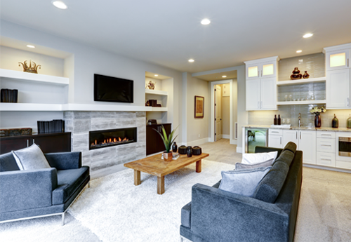Modernes Wohnzimmer mit Kamin, grauen Sofas, flauschigem Teppich und offener Küchenzeile in Weiß mit Glaselementen.