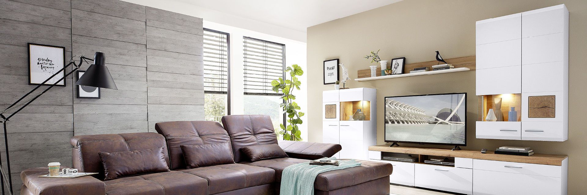 Modernes Wohnzimmer mit brauner Ledercouch, TV und weißen Regalen.
