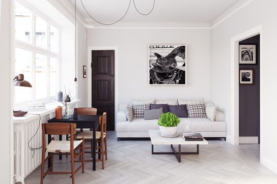Helles Wohnzimmer mit weißem Sofa, schwarz-weißer Kunst an der Wand und kleiner Essecke mit vier Holzstühlen.