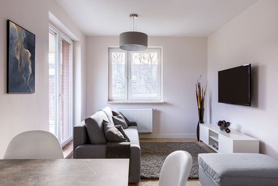 Heller, moderner Wohnraum mit grauem Sofa, Wand-TV und Esstisch im Vordergrund.