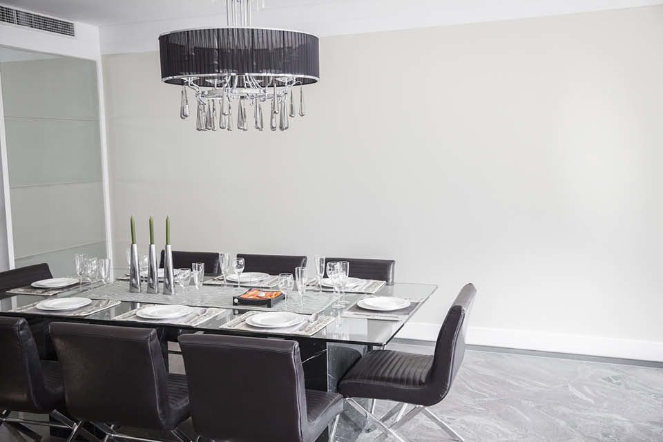 Eleganter Essbereich mit Glas-Esstisch, modernen schwarzen Stühlen und stilvoller Hängelampe mit Tropfenanhängern – minimalistisch und edel gedeckt.