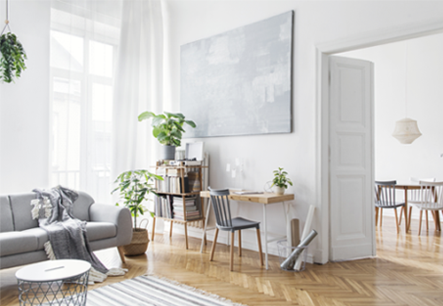 Heller, skandinavisch eingerichteter Wohnraum mit grauem Sofa, Holzmöbeln, Zimmerpflanzen und Wandbild in gedeckten Farben.