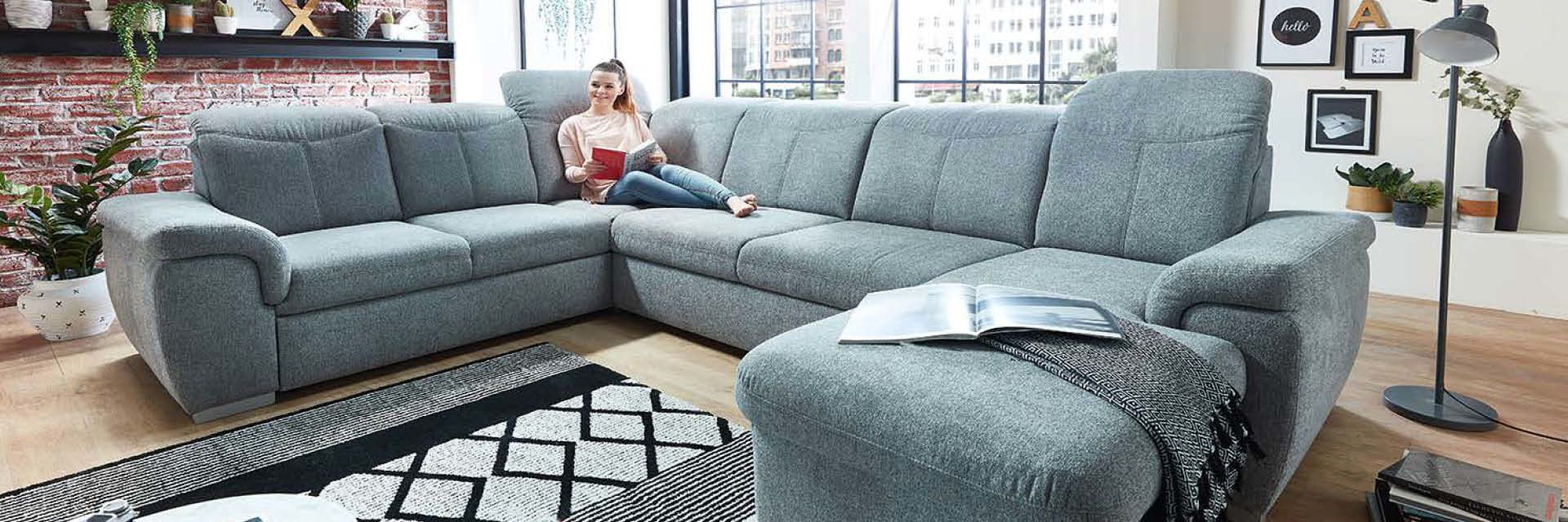 Eine graue Eckcouch mit einer Frau, die auf der Couch sitzt und ein Buch liest.