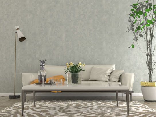 Modern eingerichtetes Wohnzimmer mit hellem Sofa, Stehlampe, Zimmerpflanze und einem dekorierten Couchtisch auf gemustertem Teppich.