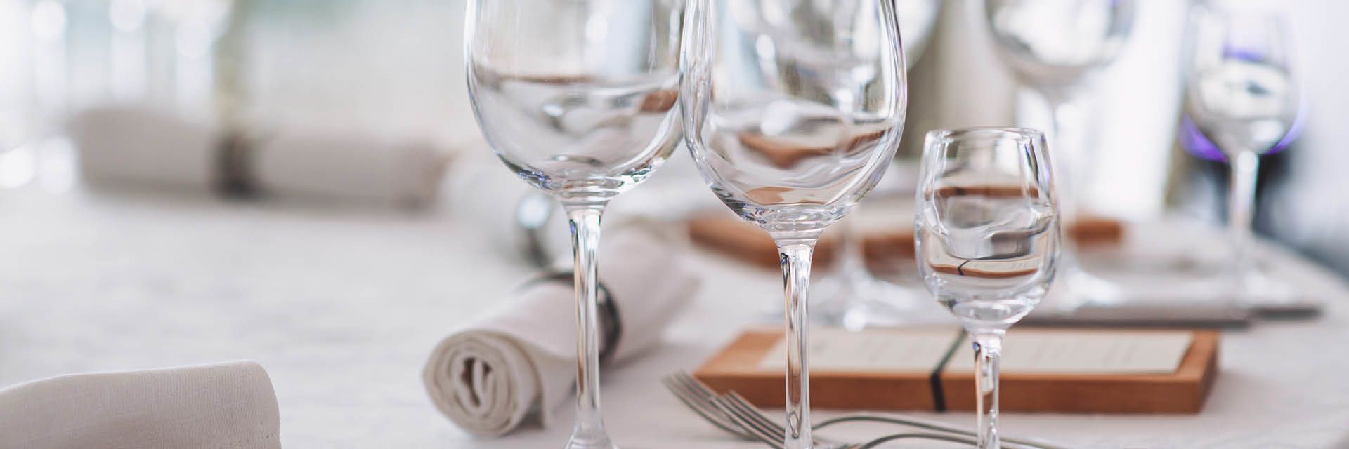 Elegant gedeckter Tisch mit klaren Weingläsern, Stoffservietten und Menükarten – stilvolle Vorbereitung für ein feines Dinner.
