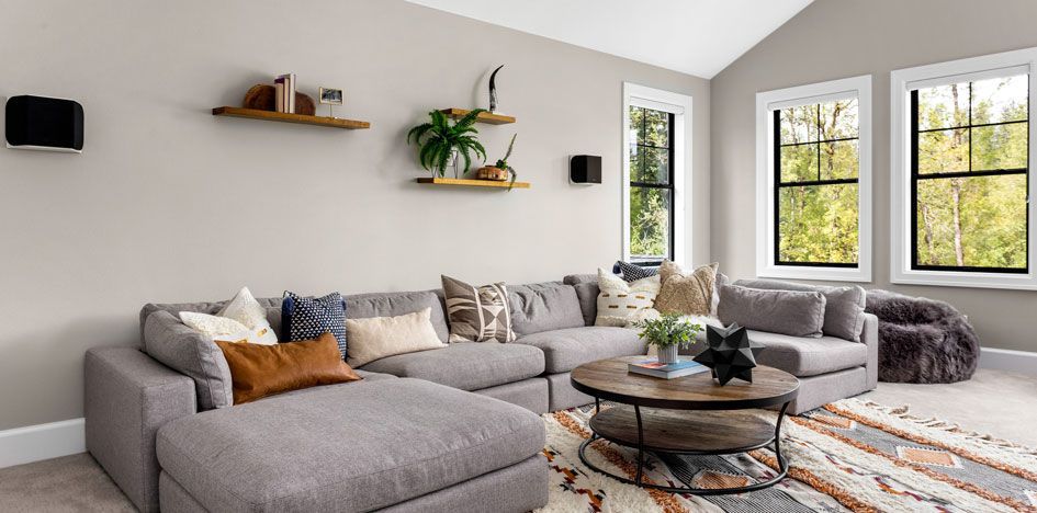 Gemütliches Wohnzimmer mit grauem Ecksofa, Couchtisch und Pflanzenregalen.