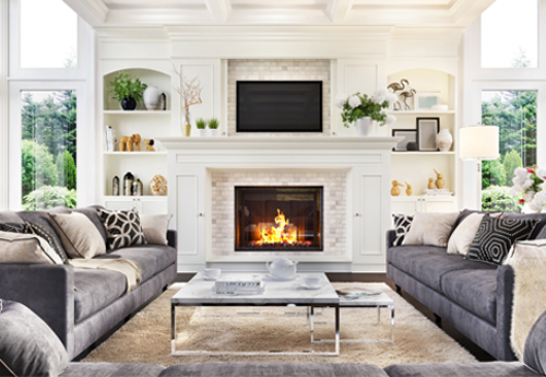 Helles Wohnzimmer mit Kamin, zwei grauen Sofas, weißem Regal mit Deko und zentralem Couchtisch aus Glas.