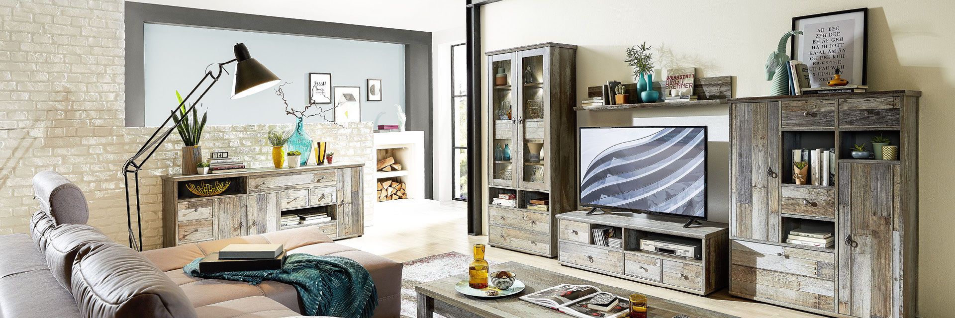 Wohnzimmer mit grauem Sofa, rustikalem TV-Möbel und Backsteinwand.