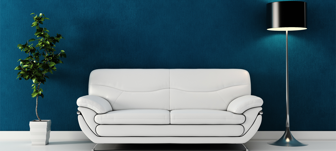 Weißes Sofa vor einer blauen Wand, daneben ein kleiner Baum und eine Stehlampe.