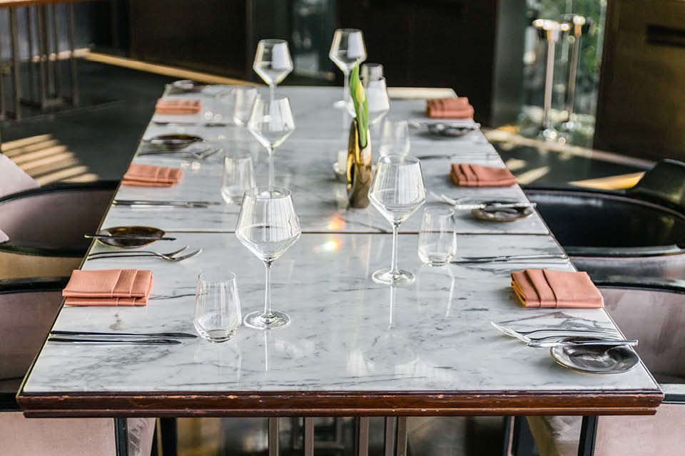 Moderner Marmortisch stilvoll gedeckt mit Weingläsern, Stoffservietten in Altrosa und goldener Blumenvase als eleganter Mittelpunkt.