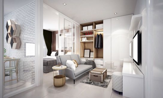 Helles, modernes Apartment mit kleinem Wohnbereich, grauem Sessel, offener Garderobe und Blick ins Schlafzimmer.