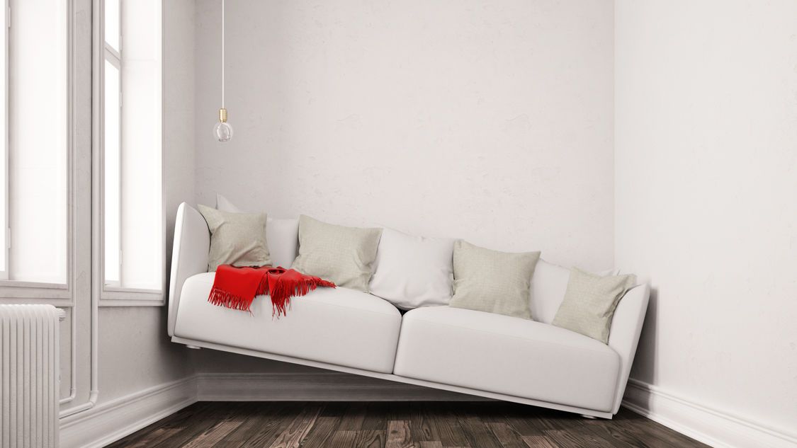 Weißes Sofa in einer Zimmerecke, schräg an die Wand gelehnt, mit hellen Kissen und rotem Tuch als Akzent.
