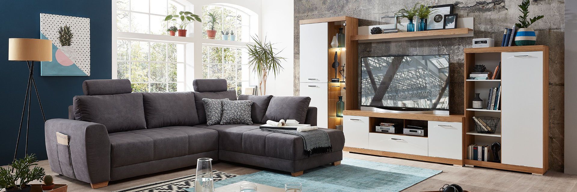Wohnzimmer mit grauem Sofa, modernem TV-Möbel, Pflanzen und großer Fensterfront.