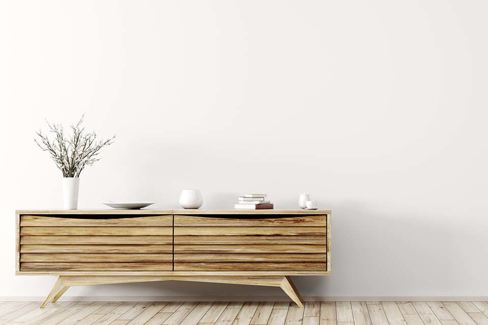 Schlichtes Sideboard aus hellem Holz im Mid-Century-Stil, dekoriert mit minimalistischen Accessoires auf hellem Holzboden vor weißer Wand.