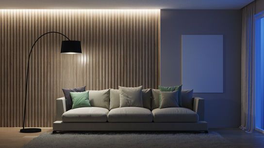 Stilvoller Wohnbereich mit großem Sofa, Stehlampe und indirekter Beleuchtung vor einer Holzpaneelwand.